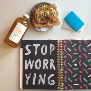 Paper planner says "Stop Worrying" with kombucha bottle and a breakfast sandwich