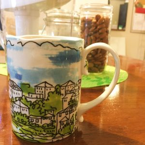 hand painted Anthropologie mug sits on a coffee table with water pitcher and nuts in a jar in the background